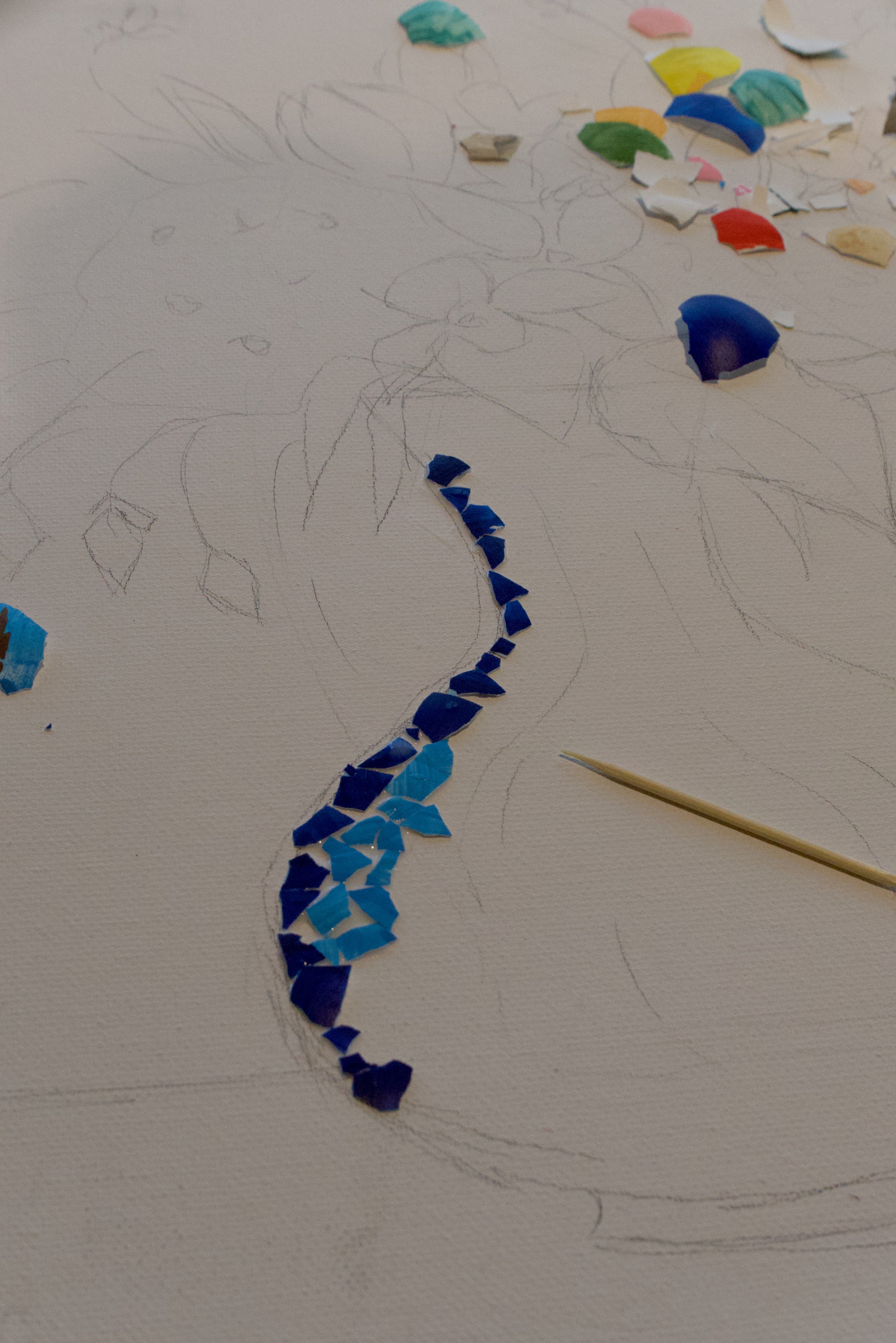Close-up — hands placing blue eggshell fragments onto the glued canvas